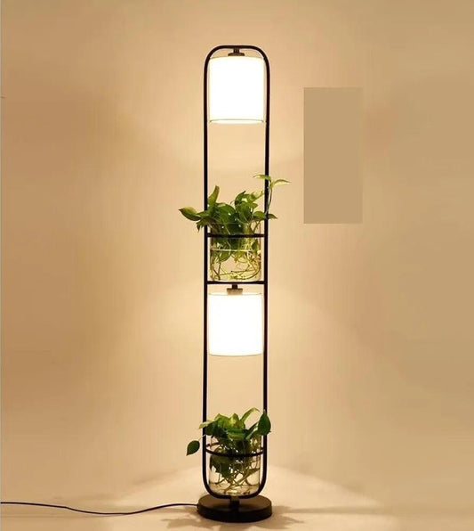 Full view of the standing floor lamp with both lights turned on, showcasing plants in glass pots and warm illumination in a modern room.