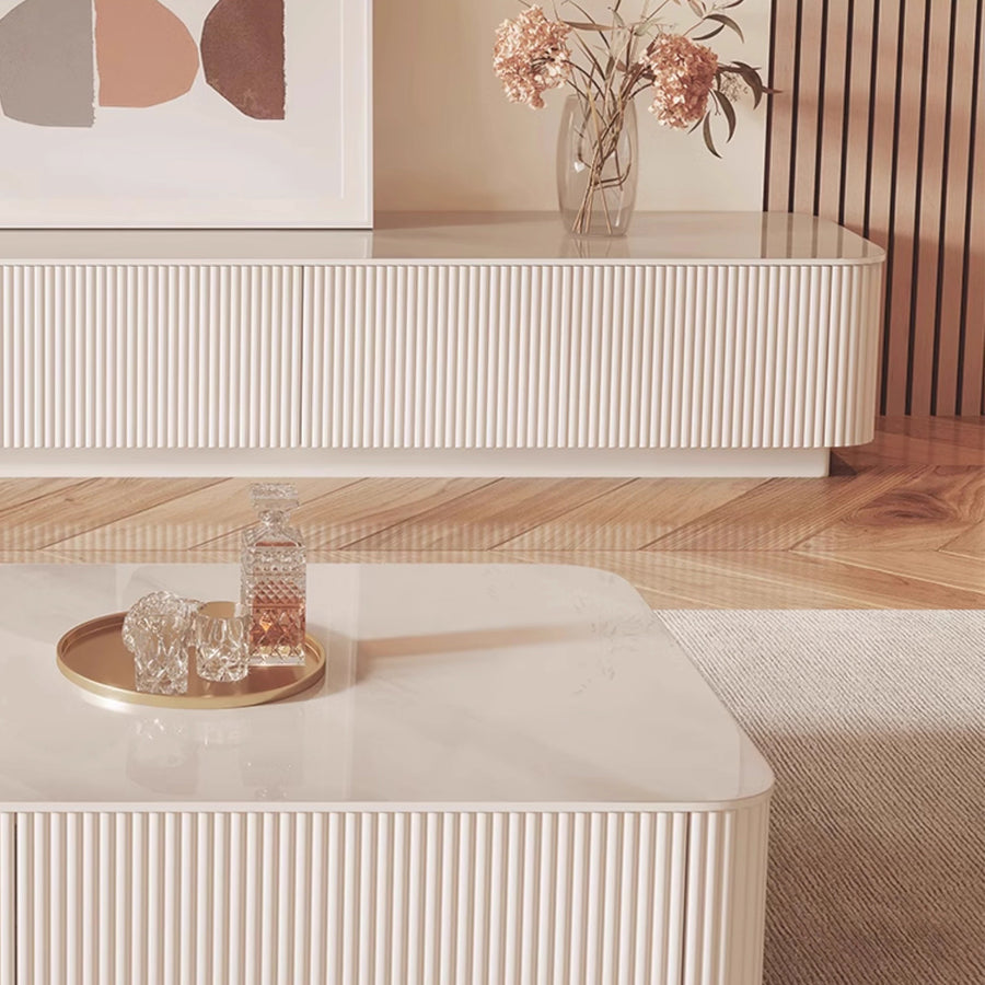 Modern living room with white furniture, a vase of flowers, and abstract art on the wall.