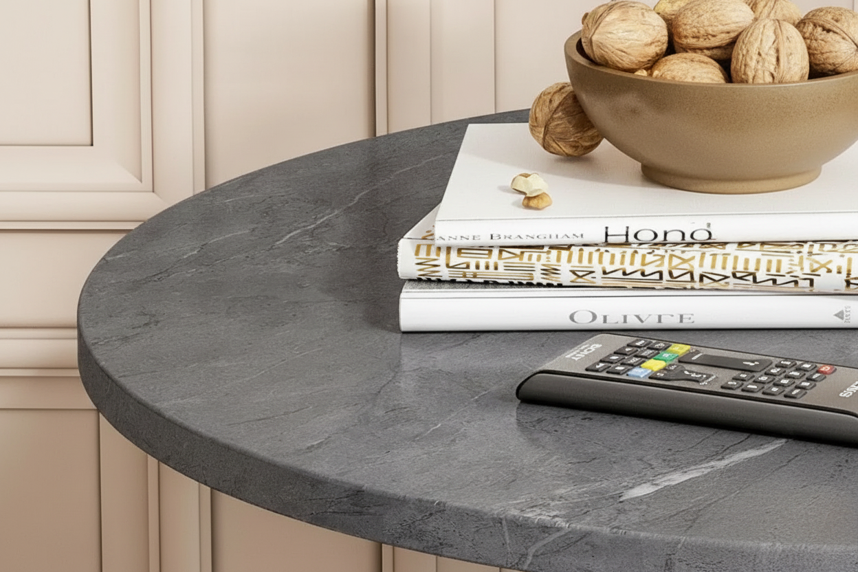 Round dark gray stone countertop with books and a remote control on top, against a beige wall.